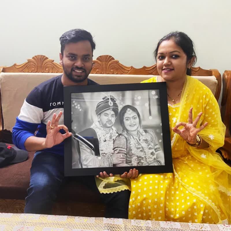 A couple sitting on a sofa holding a framed pencil portrait of their wedding photograph, both giving a thumbs-up.